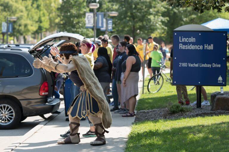 families unload belongings from cars on move-in day outside of Lincoln Residence Hall, while mascot Orion cheers on