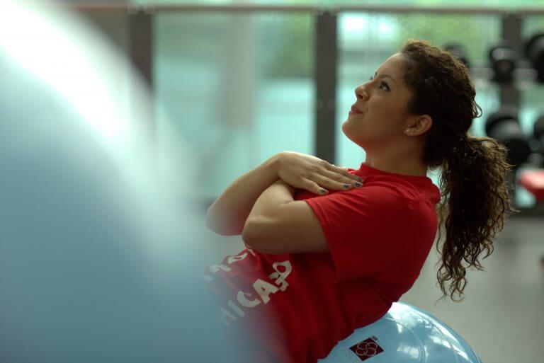female in pony tail and T'shirt doing situps against a rubber ball